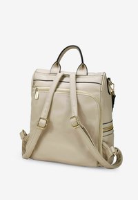 Zaino in pelle beige con doppi manici superiori e spallacci regolabili. Presenta dettagli in metallo dorato e tasche anteriori con cerniera.