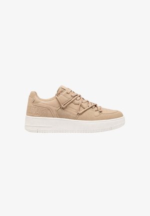 Zapatilla beige de perfil bajo con paneles texturizados, perforaciones, suela blanca gruesa y cordones, vista lateral sobre fondo blanco.
