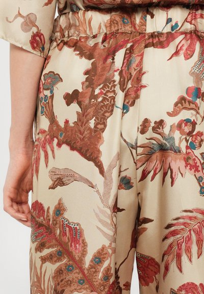 Blomsterjumpsuit i lys beige med detaljerede mønstre i brun, blå og pink. Blød tekstur med elastisk talje og brede ærmer.
