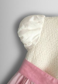 Weißer, strukturierter Miederteil mit einem zarten rosa Satinbund, der in einen fließenden rosa Rock übergeht. Puffärmel aus glänzendem weißem Stoff.