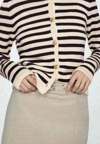 Cardigan a righe in beige e blu navy, con bottoni dorati, texture a maglia e maniche lunghe, abbinato a una gonna di colore chiaro.
