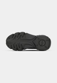 Zwarte sneakerzool van getextureerd rubber, met opvallende profielpatronen en een circulair logo. Gebogen en gestroomlijnd ontwerp.