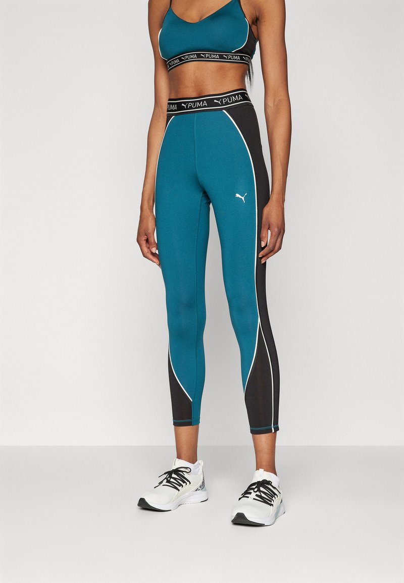 Leggings turchesi e neri con bordature bianche, realizzati in materiale elasticizzato. Abbinati a un reggiseno sportivo nero con fascia con logo.