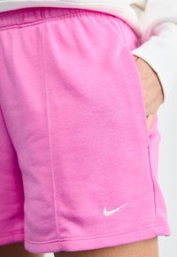 Rosa bomullsshorts med elastiskt midjeband. Har sidofickor och en liten vit Nike-logotyp nederst. Mjuk textur och avslappnad passform.
