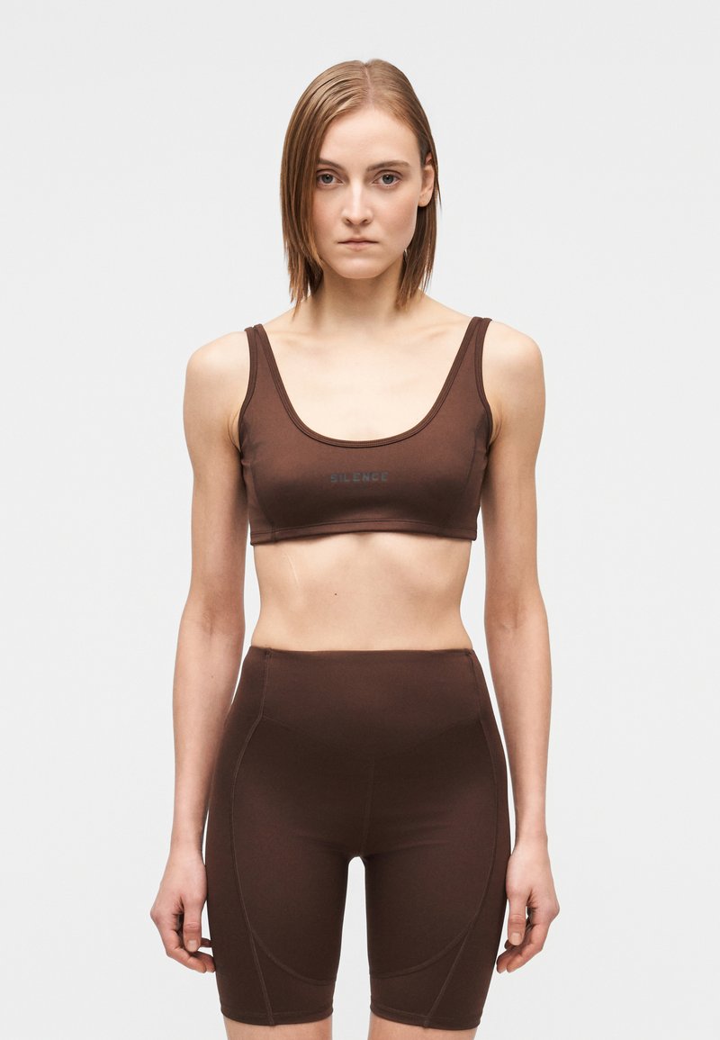 Barna aktív ruhaszett, amely egy ujjatlan haspólót tartalmaz kerek nyakkivágással és magas derekú, szűk szabású nadrágot varrási részletekkel.