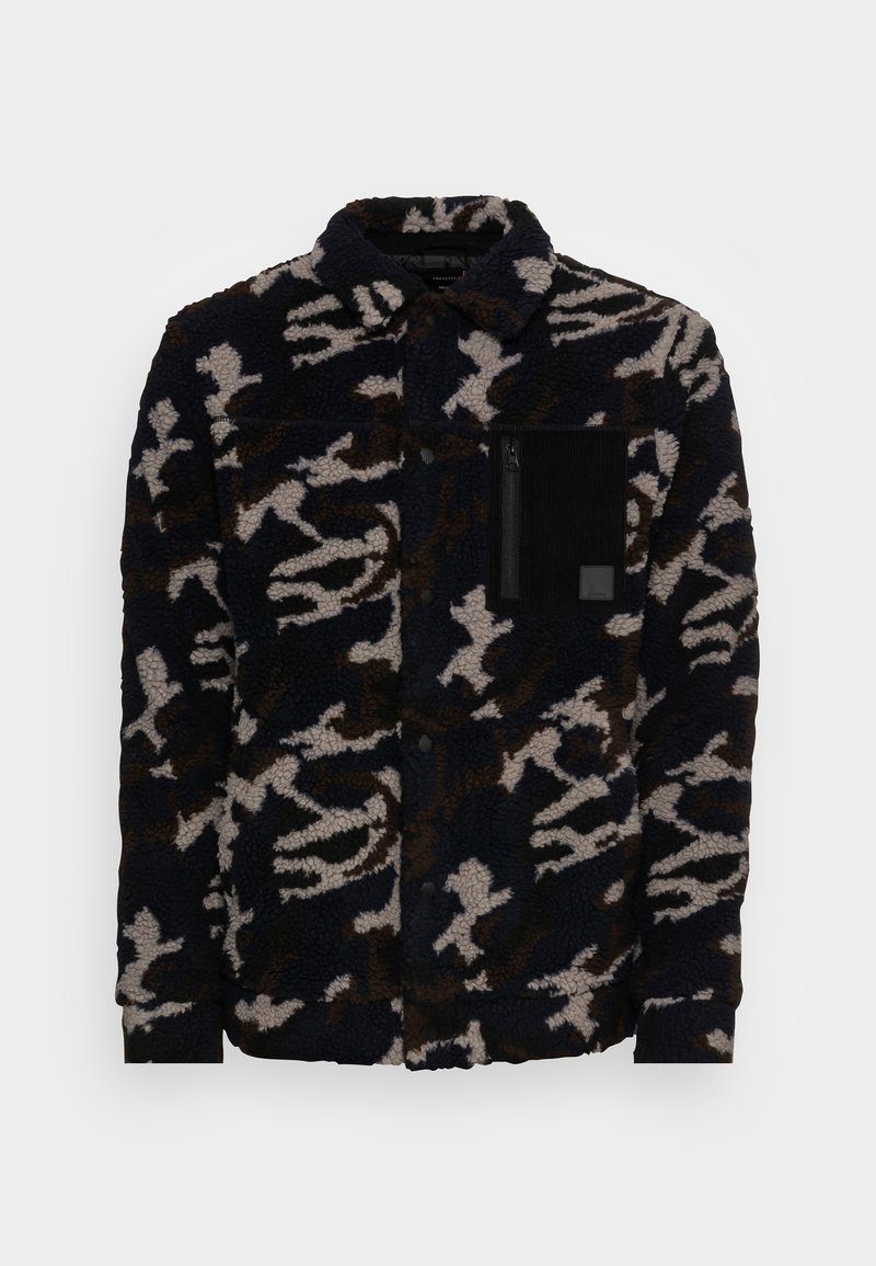 Veste en polaire bleu marine foncé avec un motif camouflage abstrait beige et marron. Elle comprend une poche plaquée avec fermeture éclair sur la poitrine.