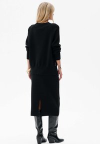 Czarny sweter z dzianiny z raglanowymi rękawami, w zestawieniu z dopasowaną czarną spódnicą z rozcięciem z tyłu, noszoną z czarnymi kozakami na wysokim obcasie do kolan.