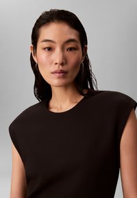 Svart ermeløs topp med rund hals og strukturert skulderdesign. Jevnt stoff med en subtil glans.