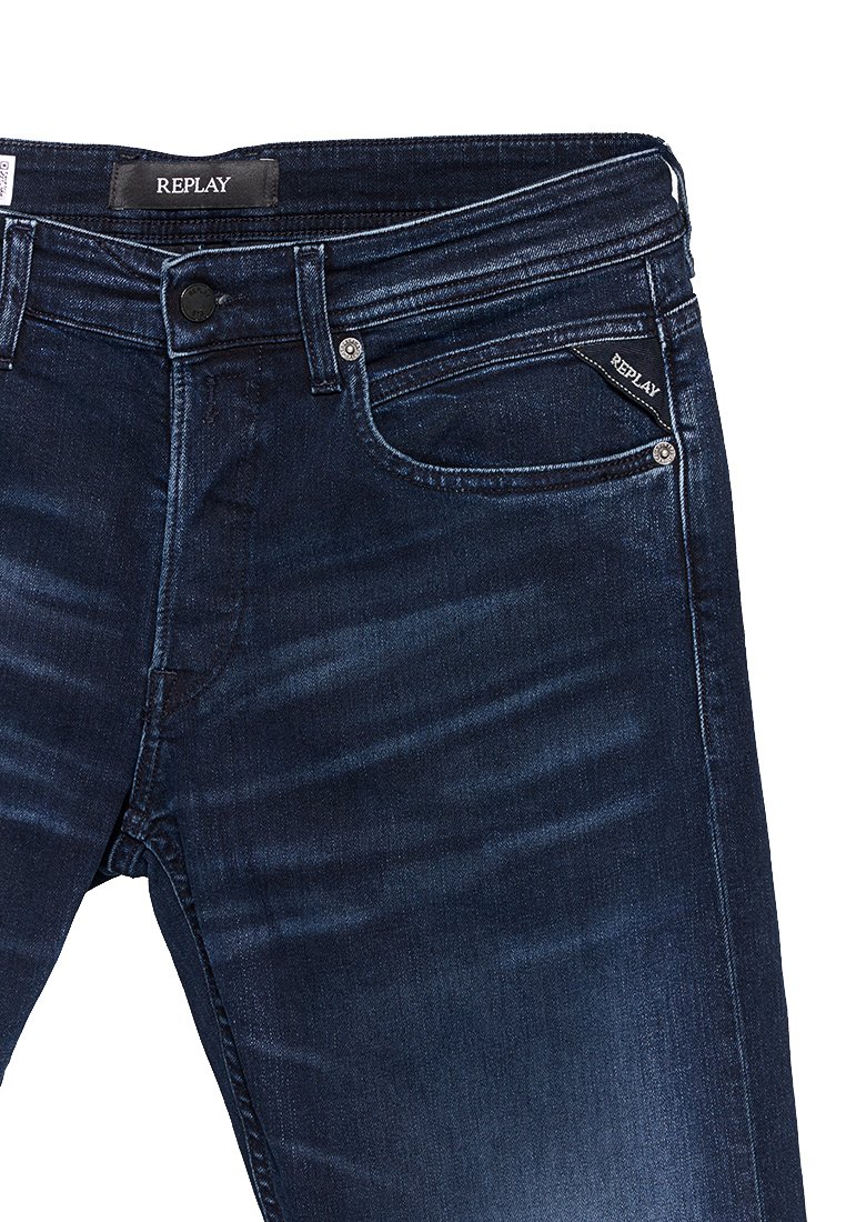 Donkerblauwe denim jeans met een lichte vervaging, voorzien van een ritssluiting, vijf zakken en een label met de tekst "REPLAY" op de tailleband.