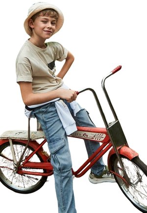 Bicicletta vintage rossa con un sedile bianco e manopole in cromo. Una persona giovane indossa una camicia beige e jeans di denim, posando con sicurezza.