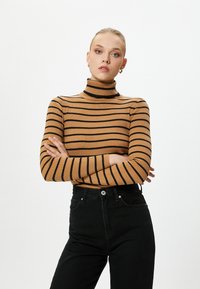 Brauner gerippter Rollkragenpullover mit schwarzen Streifen, taillierte Passform, lange Ärmel, kombiniert mit hochgeschnittenen schwarzen Jeans. Keine bemerkenswerten Akzente.