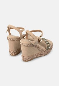 Sandales compensées beige avec une semelle en jute tressé, un dessus en daim, une sangle de cheville réglable et des détails embellis à l'avant.