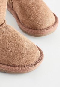 Tan mockaskinn ankelboots med rund tå, texturerad yta och sömnad detaljer runt kanten och sulan, med en mjuk foder.