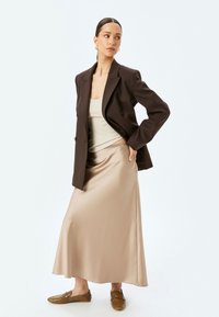 Brun dobbeltbrystet blazer over en beige tætsiddende tanktop og satin beige maxi nederdel, parret med teksturerede brune slip-on sko.