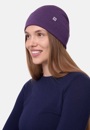Lilla strikket hue med en glat tekstur og et lille logo mærke, båret af en smilende person med glat hår, iført en marineblå skjorte.
