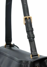 Zwarte leren handtas met een plat ontwerp, verstelbare strap met gouden hardware en een gladde textuur. Accenten zijn onder andere stiksels.