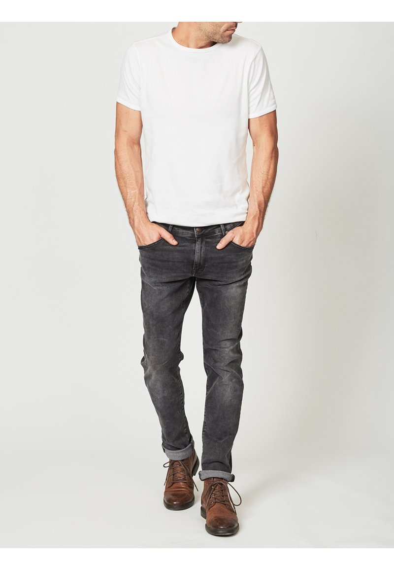 Vit t-shirt med kort ärm i kombination med mörkgrå slim-fit jeans och bruna snörskor; avslappnad outfit med en enkel, ren design.