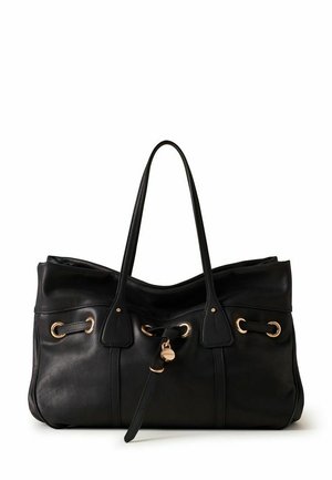 Sac à main en cuir noir avec doubles poignées, œillets dorés et une sangle décorative avec un pendentif rond en or au centre devant.