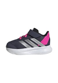 Zapatilla deportiva con una parte superior de malla en un azul marino oscuro, franjas plateadas, detalles en rosa y una correa de Velcro. Suela de goma blanca.