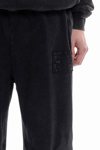 Pantalones deportivos negros hechos de tela suave, con un logo en relieve "FV" en el muslo izquierdo. Los pantalones tienen un corte relajado y cinturilla elástica.