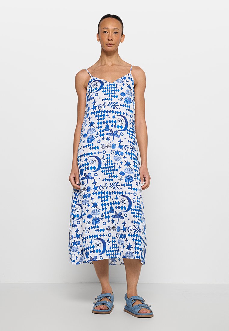 Vestido maxi de patrón azul y blanco con tirantes finos, con diseños florales y geométricos, hecho de una tela ligera, combinado con sandalias azules.
