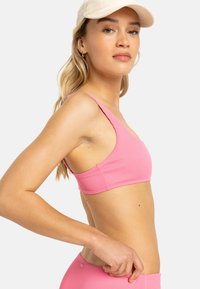 Pink ribbed sports bra with a deep scoop neckline and wide straps. The fabric has a textured finish and is designed for comfort.