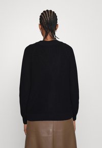 Czarny dziany sweter o prążkowanej fakturze, z długimi rękawami i okrągłym dekoltem, zestawiony z gładką brązową spódnicą skórzaną.