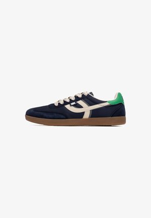 Zapatillas de gamuza azul marino con detalles en crema y lengüeta trasera verde. Suela de goma texturizada y cordones con patrón. Diseño clásico deportivo.
