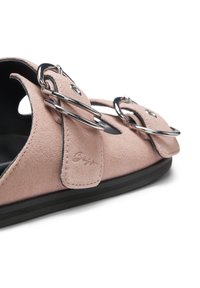 Sandale en daim rose doux avec deux boucles circulaires argentées et une semelle noire, montrant les brides latérales et supérieures.
