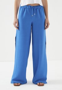Blauwe, brede broek van zachte stof met een elastische tailleband en trekkoord. Bevat zijslitsen en een soepele textuur.