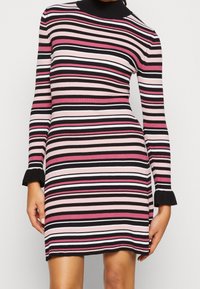 Abito a maglia a coste con collo alto finto, caratterizzato da strisce orizzontali in nero, rosa e bianco. Sottile con maniche svasate.