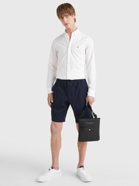 White button-up shirt, navy shorts, white sneakers, and a black bag with a zipper. Casual outfit with a clean design and contrasting colors.