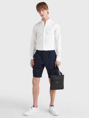 White button-up shirt, navy shorts, white sneakers, and a black bag with a zipper. Casual outfit with a clean design and contrasting colors.
