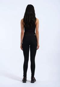 Svarta leggings gjorda av stretchigt material, med hög midja och en åtsittande design, ihop med svarta skor och en enkel klocka.