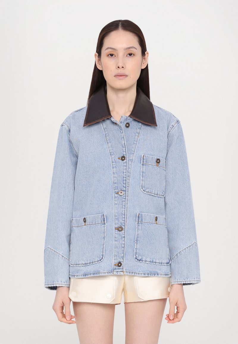 Lichtblauwe spijkerjas met een bruine leren kraag, knoopsluiting aan de voorkant, twee grote opgestikte zakken en lange mouwen met een relaxte pasvorm.