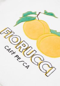 Pêches jaunes avec des feuilles vertes brodées au-dessus du texte "FIORUCCI" et "CAFÉ PESCA" sur un fond en tissu blanc.
