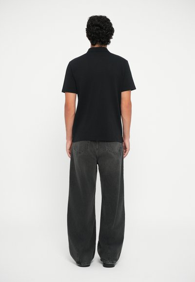 Must põlvaga T-särk, valmistatud puuvillast, koos lahti lõige tumeda halli teksapükstega, millel on nähtavad tagataskud.