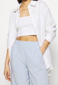 Witte linnen blouse over een witte crop top, gecombineerd met lichtblauwe en witte gestreepte wijde broek met zijzakken.