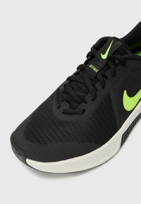 Sorte atletiske sneakers med en mesh-overdel, lys grønne accenter, tekstureret tåhætte og en gummisål. Snøre-design.