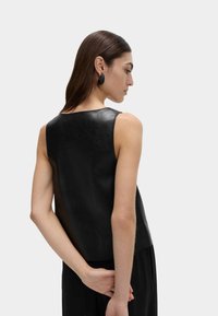 Top negro sin mangas de cuero con una textura lisa, que presenta un corte recto y un escote redondeado. Combinado con pantalones negros.