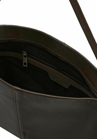 Ciemnobrązowa skórzana torba na ramię z widoczną przednią kieszenią, zamkiem błyskawicznym i regulowanym paskiem na białym tle.