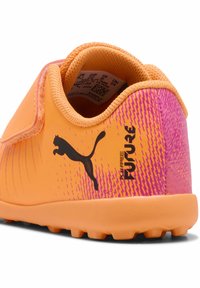Scarpa da calcio arancione e rosa con parte superiore in sintetico testurizzato, cinturino in velcro e logo Puma nero. Include un design a fantasia e suola in gomma.