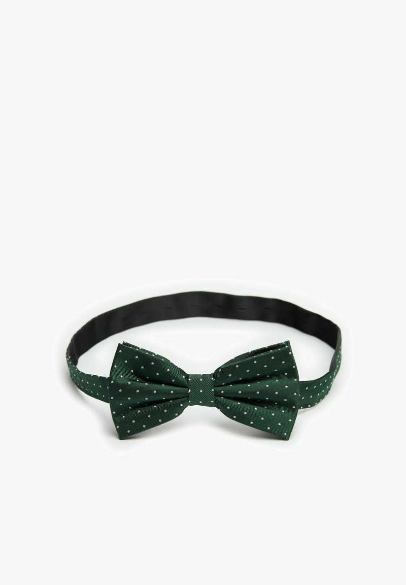 Vihreä pilkullinen solmio, joka on valmistettu tekstiili-materiaalista, leveällä solmulla ja mustalla säädettävällä hihnalla.