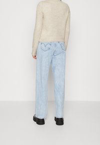 Light blue wide-leg jeans with a faded finish, featuring stitched back pockets and a red logo tag, paired with a beige knitted sweater.
