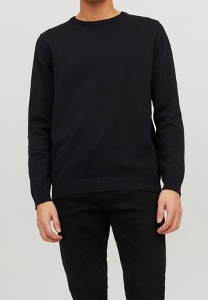 Pull en tricot bleu marine à manches longues, col rond, avec des poignets et un ourlet côtelés, fabriqué en tissu doux, porté avec un pantalon noir.