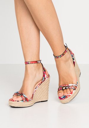 Sandaletter med kilehæl, der har et overdel i multicolor blomstret stof, sorte stropper og en tekstureret jute kilehælfod. Åben tå-designet afslører malede negle.