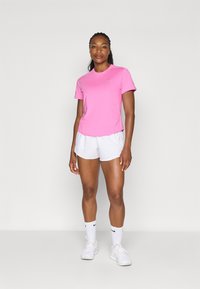 Ružová športová košela s krátkym rukávom a okrúhlym výstrihom, skombinovaná s bielymi šortkami. Model má na sebe biele tenisky a športové ponožky, čo vytvára ležérny vzhľad.