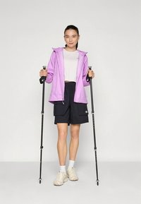 Lengvas, violetinės spalvos neperšlampamas švarkas dėvimas ant baltos palaidinės ir juodų kargo šortų; aprūpintas �žygių lazdomis ir smėlio spalvos sportbačiais.