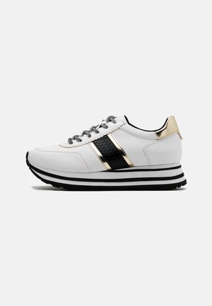 Sneaker bianca con strisce laterali nere e dorate, suola a righe nere e bianche, lacci bianchi e neri e dettaglio dorato sul tallone.