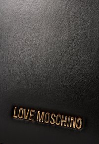 Zwarte textuurleer met een goudkleurig "LOVE MOSCHINO" logo dat prominent is weergegeven. Het oppervlak heeft een pebbled afwerking.
